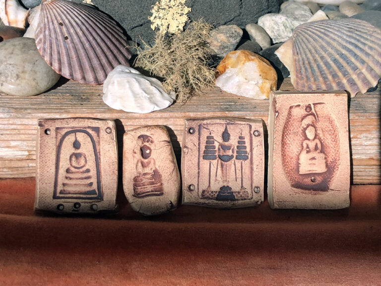 photograph of clay tiles with images of buddhas and stupas on a wooden background with shells and moss nearby